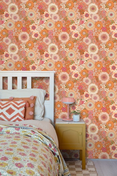 Tapete mit floralem Retro Muster als Wandgestaltung im Schlafzimmer hinter einem weißen Bett mit Nachttisch und Tischlampe.