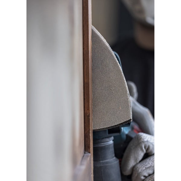 Mann schleift Holz mit einem Schwingschleifer, inklusive Schutzbrille und Staubmaske für sicheres Arbeiten.