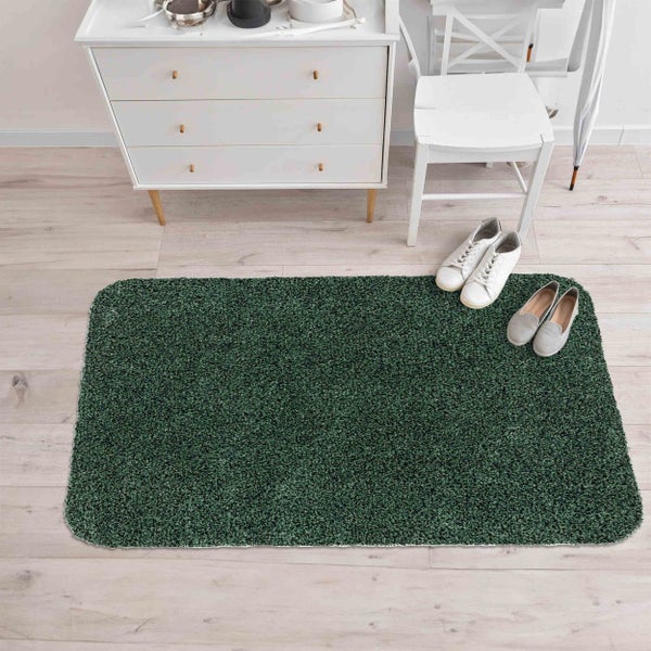 Rechteckiger, dunkelgrüner Hochflor-Teppich auf hellem Holzboden in einem hellen Zimmer mit weißer Kommode, Stuhl und Schuhen.
