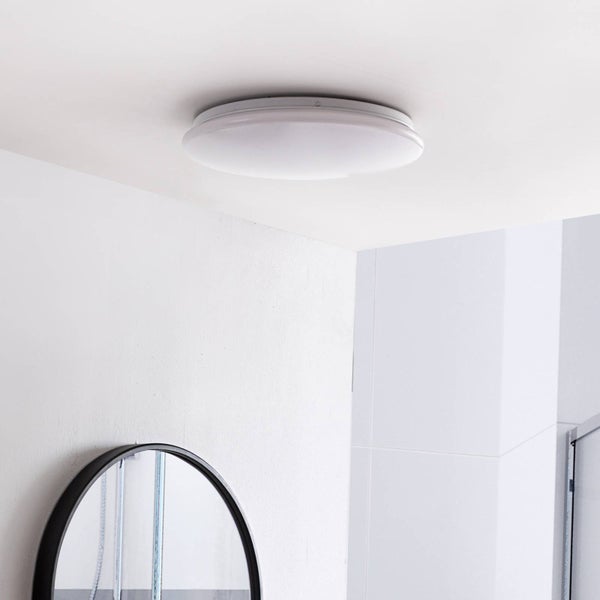 Runde Deckenleuchte für das Badezimmer, an einer weißen Decke montiert, mit einem Teil eines runden Spiegels im Vordergrund.