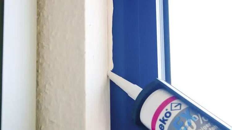 Auftragen von weißem Dichtstoff mit einer Kartuschenpresse zwischen Wand und Fensterrahmen.