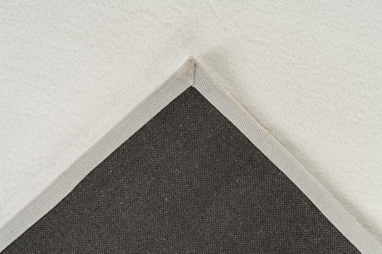 Detailansicht einer Teppichecke mit weicher Oberfläche und strukturierter dunkler Rückseite mit Webbordüre.