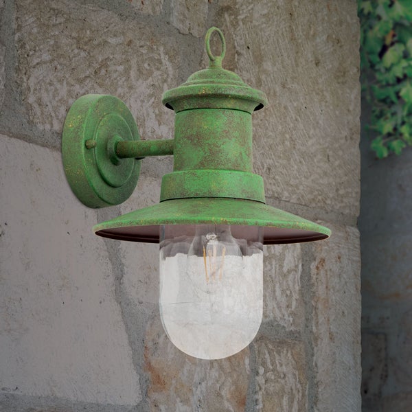 Rustikale Außenwandleuchte aus Metall mit Patina-Effekt und klarem Glas an einer Natursteinwand.