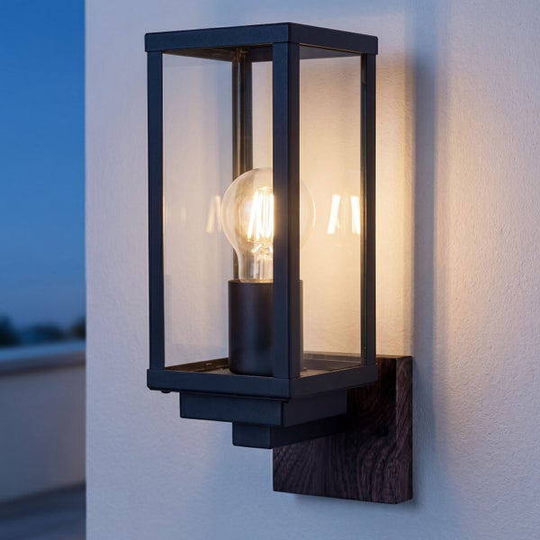 Moderne rechteckige Außenwandleuchte aus schwarzem Metall und Glas mit Holzsockel und leuchtendem LED-Leuchtmittel an einer Wand.