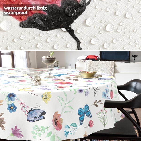Wasserundurchlässige Tischdecke mit Blumen- und Schmetterlingsmotiven auf einem runden Tisch in einem hellen Wohnzimmer.