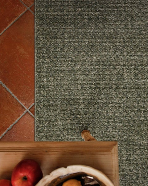 Gewebter In- und Outdoor-Teppich in strukturierter Optik auf Terrakottafliesen neben einem Holztisch.