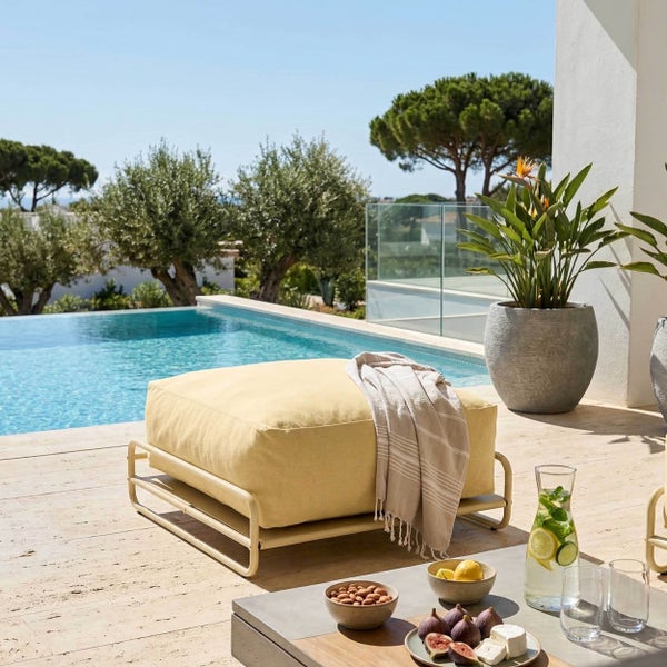 Gelber Gartenhocker auf Metallgestell neben einem Pool mit dekorierter Kaffeetafel und Pflanzgefäß im Hintergrund.