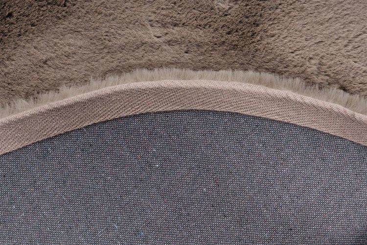 Detailansicht eines Kunstfellteppichs mit weichem Flor, gewebter Einfassung am Rand und strukturierter Rückseite.