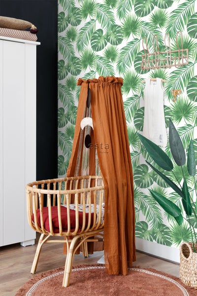 Dekoriertes Kinderzimmer mit Babybett, Baldachin und Deko-Elementen vor einer Tapete mit Pflanzenmotiven