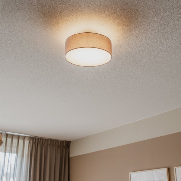 Runde Deckenleuchte mit Textilschirm montiert an einer Decke in einem hellen Raum mit Vorhängen.