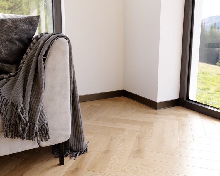 Detailansicht eines Wohnzimmers mit Parkettboden, Fußleisten und einem Sofa mit Kissen und Decke