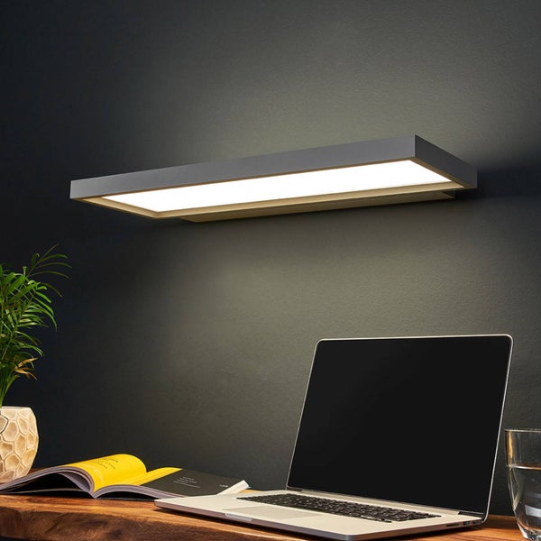 Moderne rechteckige graue LED Wandleuchte über einem Holzschreibtisch mit Laptop, Buch und Pflanze, die helles Licht auf den Arbeitsplatz wirft.
