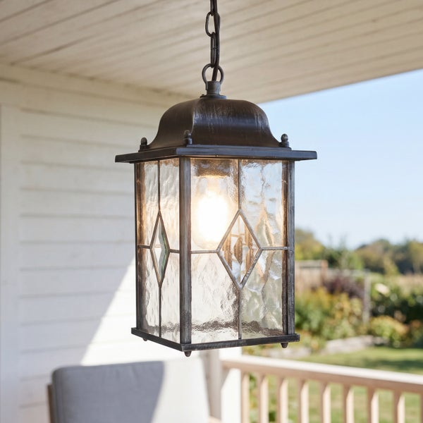 Hängende Außenleuchte im antiken Design aus Metall und strukturiertem Glas mit Rautenmuster, leuchtend auf einer Terrasse.