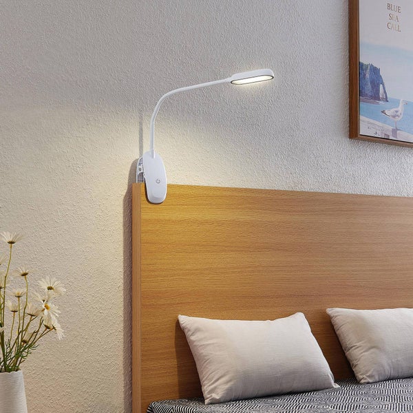 Weiße LED-Klemmleuchte mit flexiblem Arm, befestigt an einem hölzernen Kopfteil im hellen Schlafzimmer.