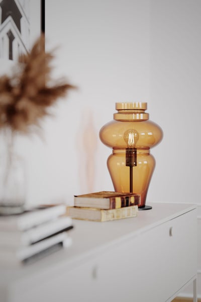 Dekorative Tischleuchte aus Glas auf Kommode mit Büchern