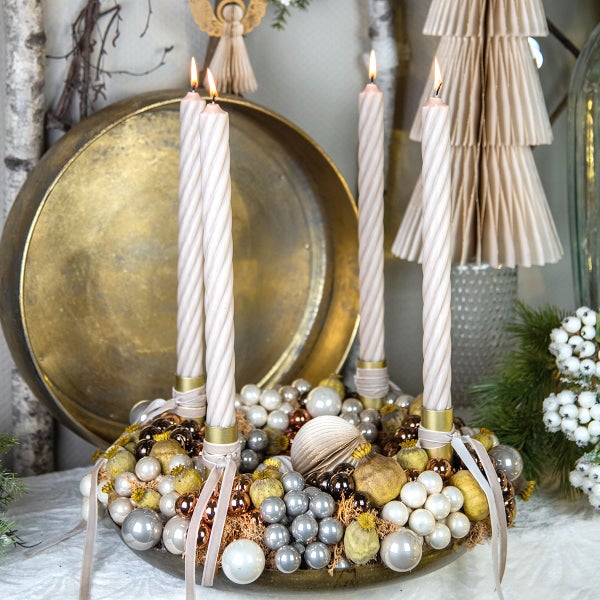 Adventskranz mit vier brennenden Kerzen, Kugeln und Schleifen auf einem Tisch.