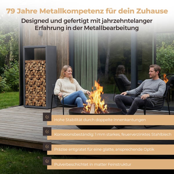 Moderne Holzterrasse mit einer schwarzen Feuerschale aus Metall und einem hohen Kaminholzregal. Ein Mann und eine Frau sitzen am Feuer.