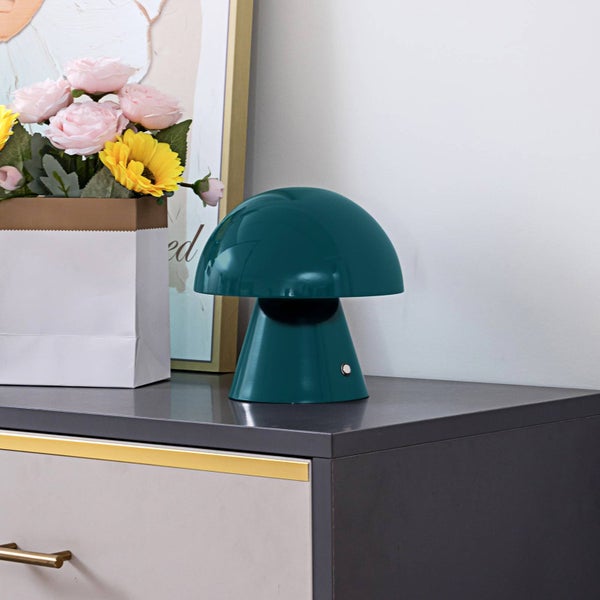 Pilzförmige Tischleuchte in Dunkelgrün auf einer modernen Kommode neben Blumen und einem gerahmten Bild.