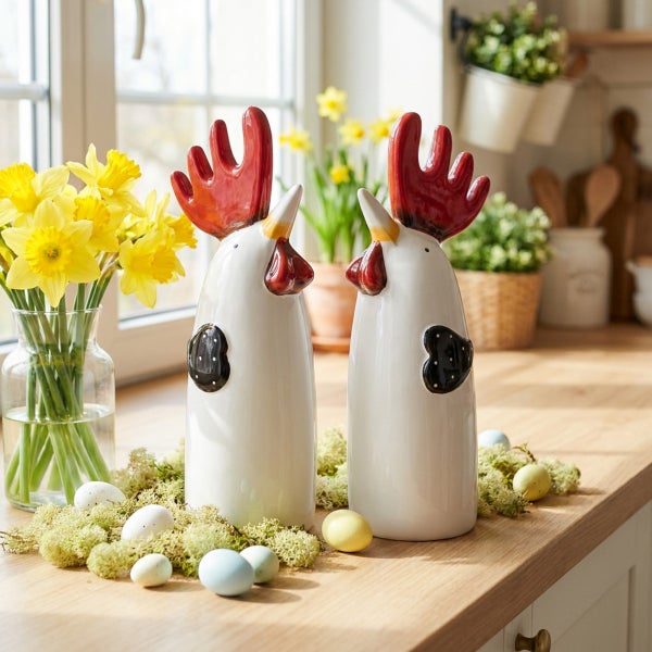 Zwei dekorative Keramik Hähne als Osterdekoration auf einer Küchenarbeitsplatte mit einer Vase voller Narzissen und kleinen Ostereiern.
