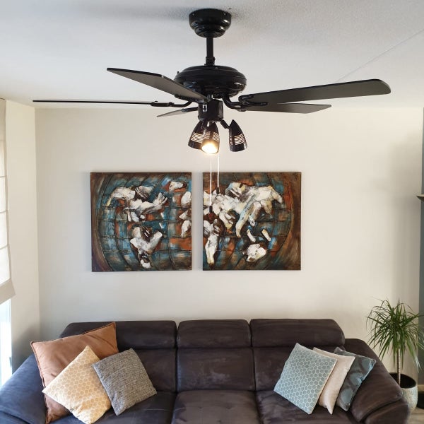 Deckenventilator mit drei Strahlern und vier Flügeln montiert in einem modernen Wohnzimmer über einem Sofa mit dekorativen Wandbildern.