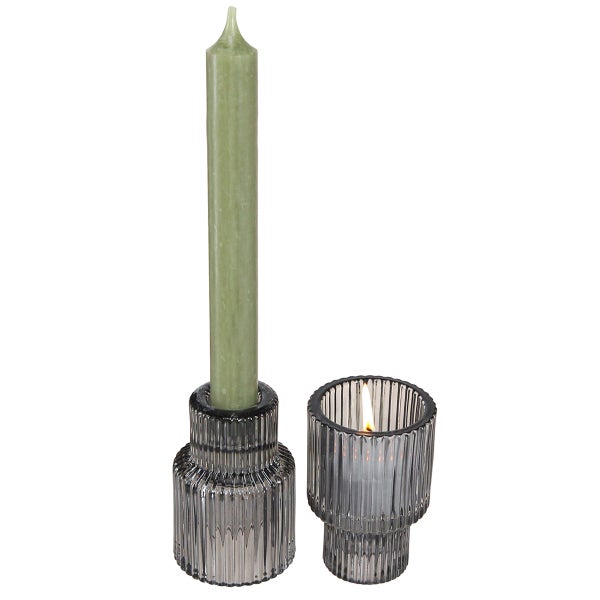 Kerzenständer aus geriffeltem Glas in Grau mit einer grünen Stabkerze und einer brennenden Kerze.
