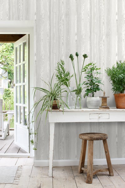 Dekoratives Zimmer mit Holzstrukturtapete, weißem Tisch und verschiedenen Pflanzen