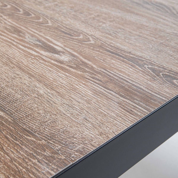 Detail einer Tischplatte in Holzoptik mit einem dunklen Metallrahmen an der Kante.