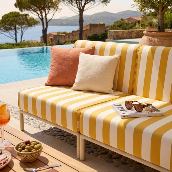 Gestreiftes Outdoor-Sofa am Pool mit Kissen, Magazin und Sonnenbrille auf einer hellen Terrasse.