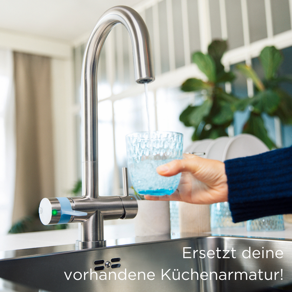 Küchenarmatur aus Edelstahl mit C-Auslauf und Filterfunktion beim Befüllen eines Glases mit Wasser in einer hellen, modernen Küche.