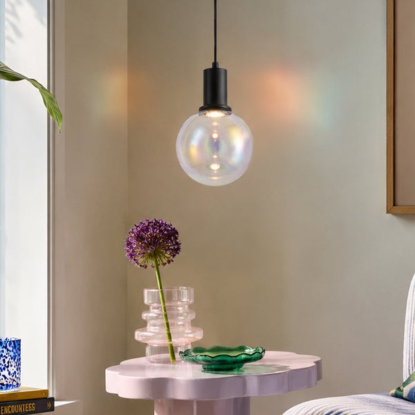 Moderne Pendelleuchte mit runder Glaskugel mit schillerndem Effekt hängend über einem kleinen Beistelltisch in einem hellen Wohnraum