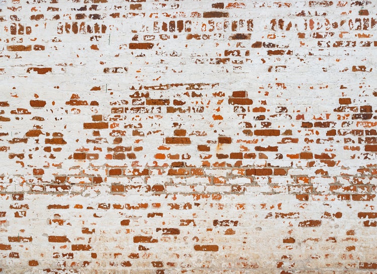 Rustikale Ziegelwand mit abblätternder weißer Farbe und sichtbarem Mauerwerk.