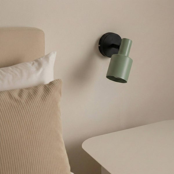 Grüne Wandleuchte neben Nachttisch und Kissen