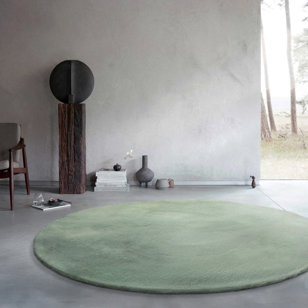 Runder, grüner Hochflor-Teppich in einem minimalistischen Wohnzimmer mit Betonboden und moderner Dekoration.