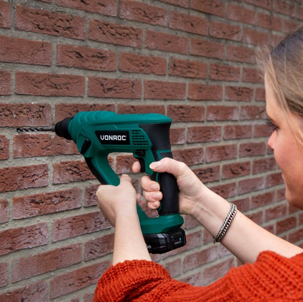 Eine Person bohrt mit einem Vonroc Akku-Bohrhammer in eine Ziegelwand.