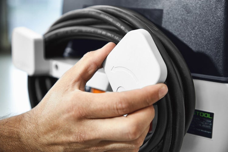 Eine Hand hält einen Stecker an einem Kabelaufroller.