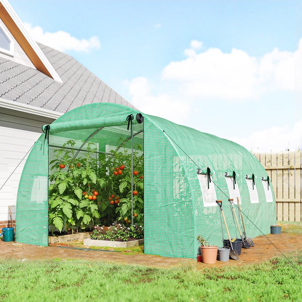 Grüner Folientunnel aus Gitterfolie im Garten mit Tomatenpflanzen, Seitenfenstern und hochrollbarer Tür, neben einem Wohnhaus platziert.