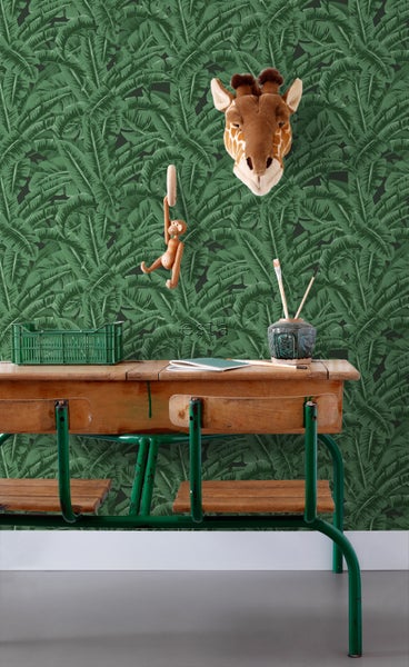 Szene mit einem Schreibtisch, einer Giraffenattrappe und einer Tapete mit tropischen Blättern.