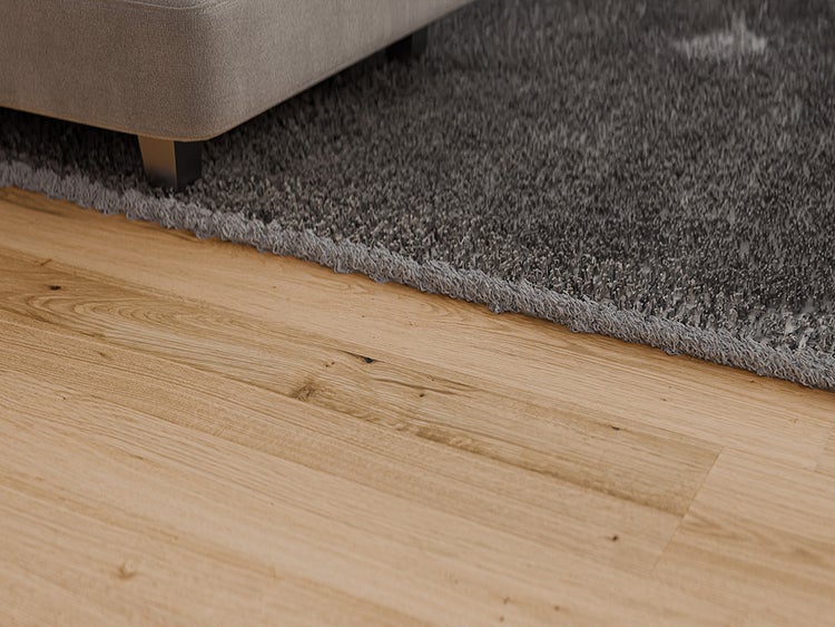 Heller Holzfußboden neben einem Hochflor-Teppich mit einem Möbelfuß aus Metall.