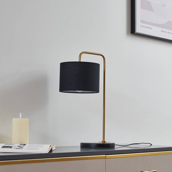 Moderne Tischleuchte mit schwarzem Textilschirm, goldfarbenem Metallgestell und schwarzem Steinfuß auf einer Kommode.