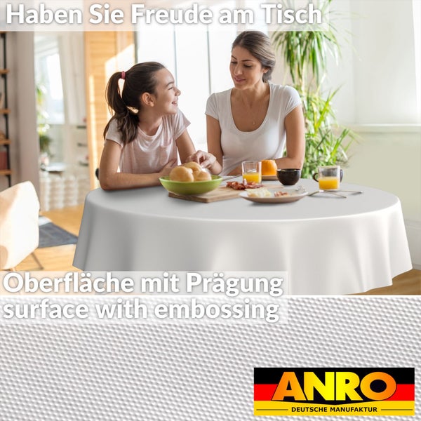 Runde weiße Tischdecke mit geprägter Oberfläche, Frau und Kind am gedeckten Esstisch in hellem Raum, ANRO Deutsche Manufaktur Logo.