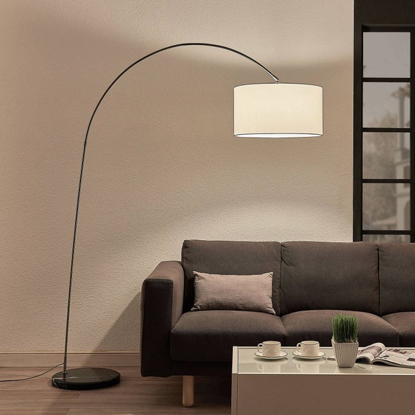 Moderne Bogenlampe mit Stoffschirm und Marmorfuß hinter einem braunen Sofa in einem hellen Wohnzimmer.