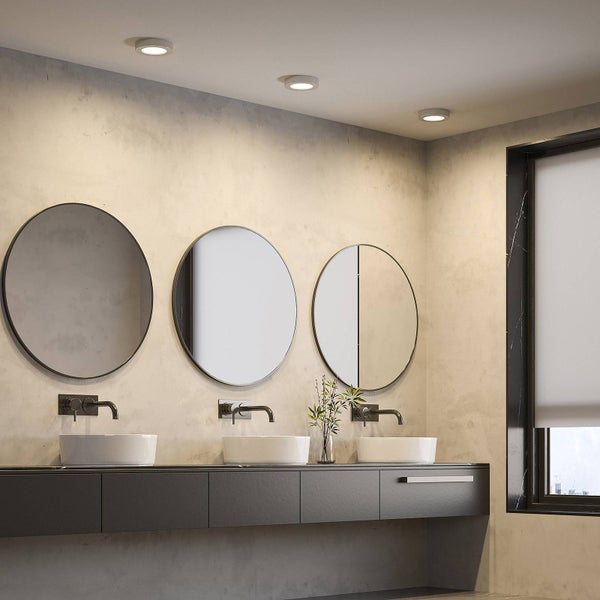 Modernes Badezimmer mit drei runden Spiegeln, drei weißen Aufsatzwaschbecken an einem dunklen Waschtisch und Deckeneinbaustrahlern.