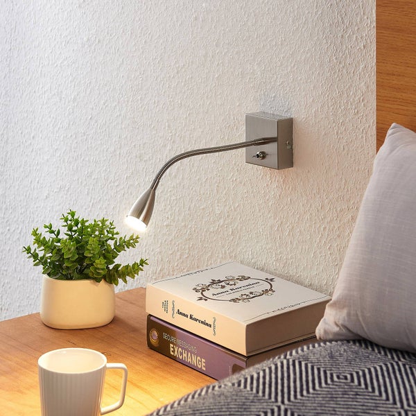Silberne LED-Wandleuchte mit flexiblem Schwanenhals, als Leselampe über einem Nachttisch mit Büchern und Pflanze montiert.