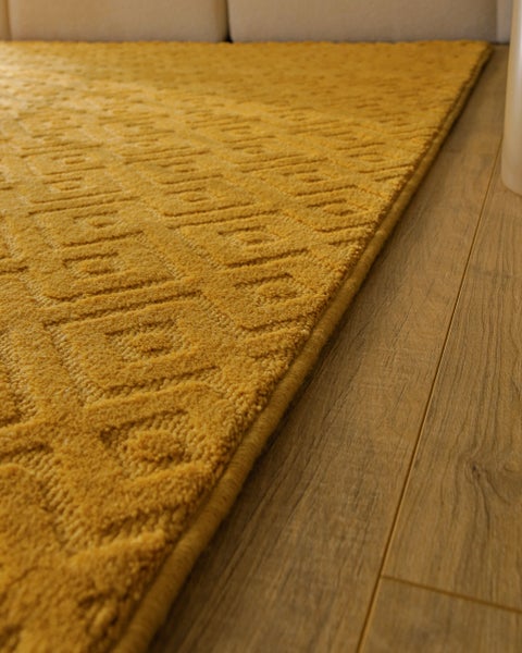 Teppich mit geometrischem Quadratmuster und Struktur im Wohnzimmer, dekoriert mit Holzhocker und offenem Buch.