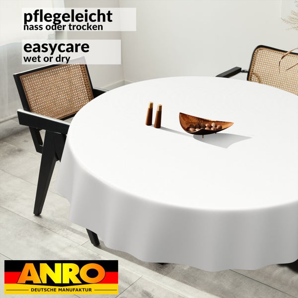 Runde, pflegeleichte Tischdecke auf einem Esstisch. Im Hintergrund stehen moderne Stühle mit Wiener Geflecht. ANRO Logo.