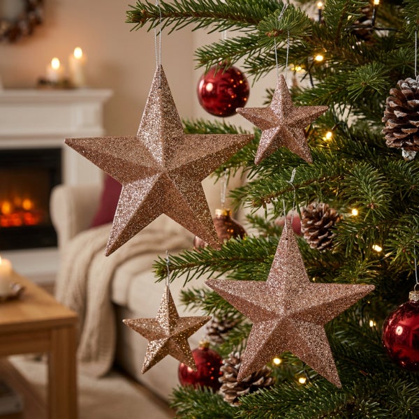 Weihnachtsbaum geschmückt mit glitzernden Sternanhängern, Tannenzapfen und Kugeln in einem wohnlich eingerichteten Zimmer mit Kamin im Hintergrund.
