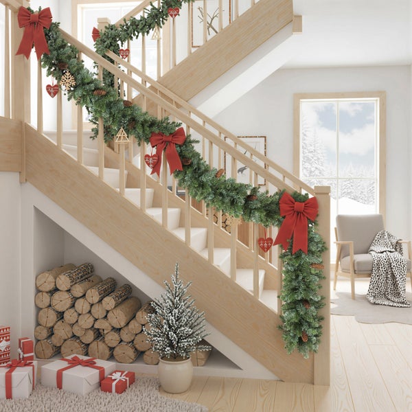 Helle Holztreppe dekoriert mit einer grünen Weihnachtsgirlande, roten Schleifen, Kaminholzstapel und kleinen Geschenken im Innenraum.
