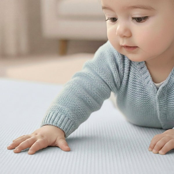 Baby in hellblauem Strickpullover auf einer hellblauen strukturierten Oberfläche in einem hellen, organisierten Wohnraum.