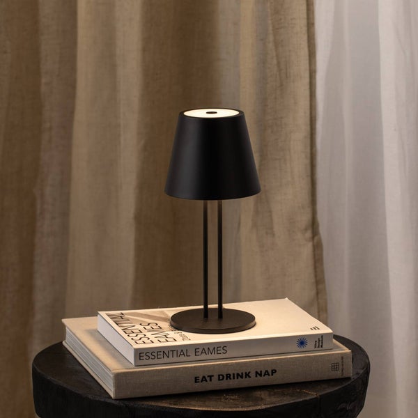Schwarze LED-Tischleuchte mit Akkubetrieb im minimalistischen Design, platziert auf Büchern vor einem Vorhang.