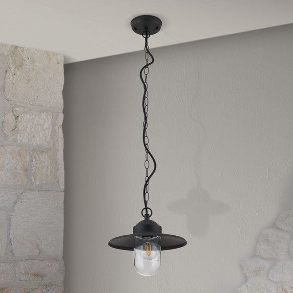 Schwarze Pendelleuchte im industriellen Design mit Metallkette und flachem Schirm, hängend von der Decke in einem Raum mit Steinmauer.